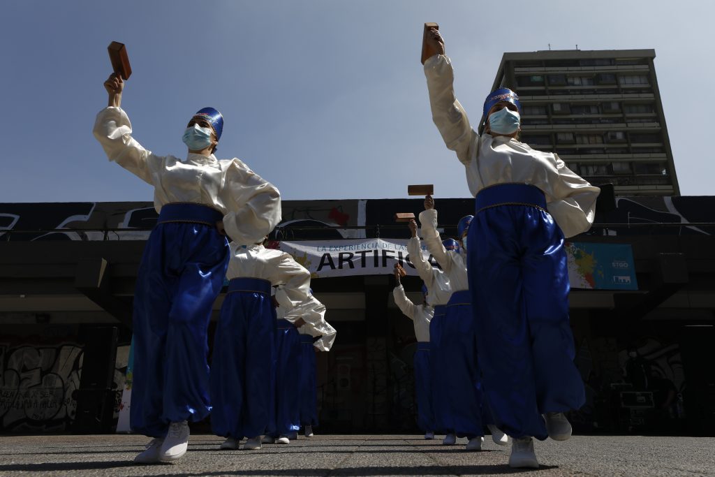 Mujeres vestidas de blanco y azul bailando. De fondo se lee Artifica tu Barrio.
